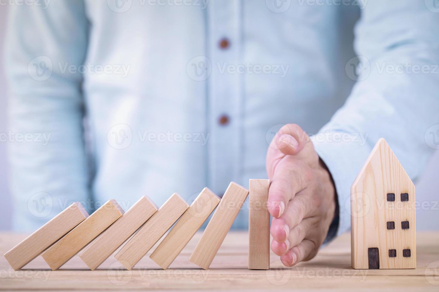 Business hands stop wooden blocks of domino effect before destroy house , Private property protection finance from domino effect concept photo