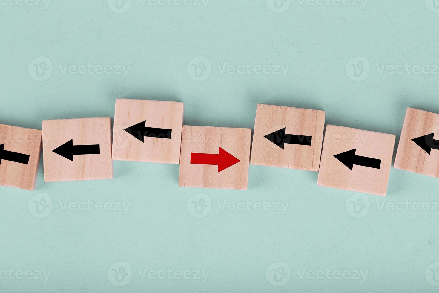 Close up wooden block on blue background with red arrow facing the opposite direction black arrows , Concept of think differently and individual photo