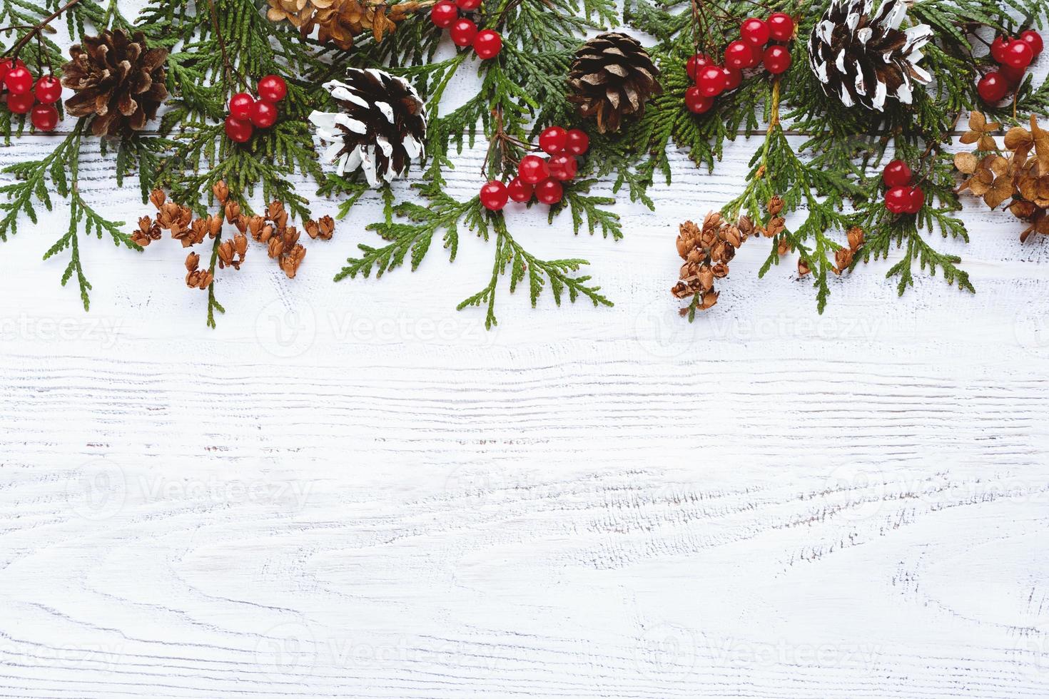 Border of Christmas tree branches pine cones flowers and red berries on white wooden background, copy space photo