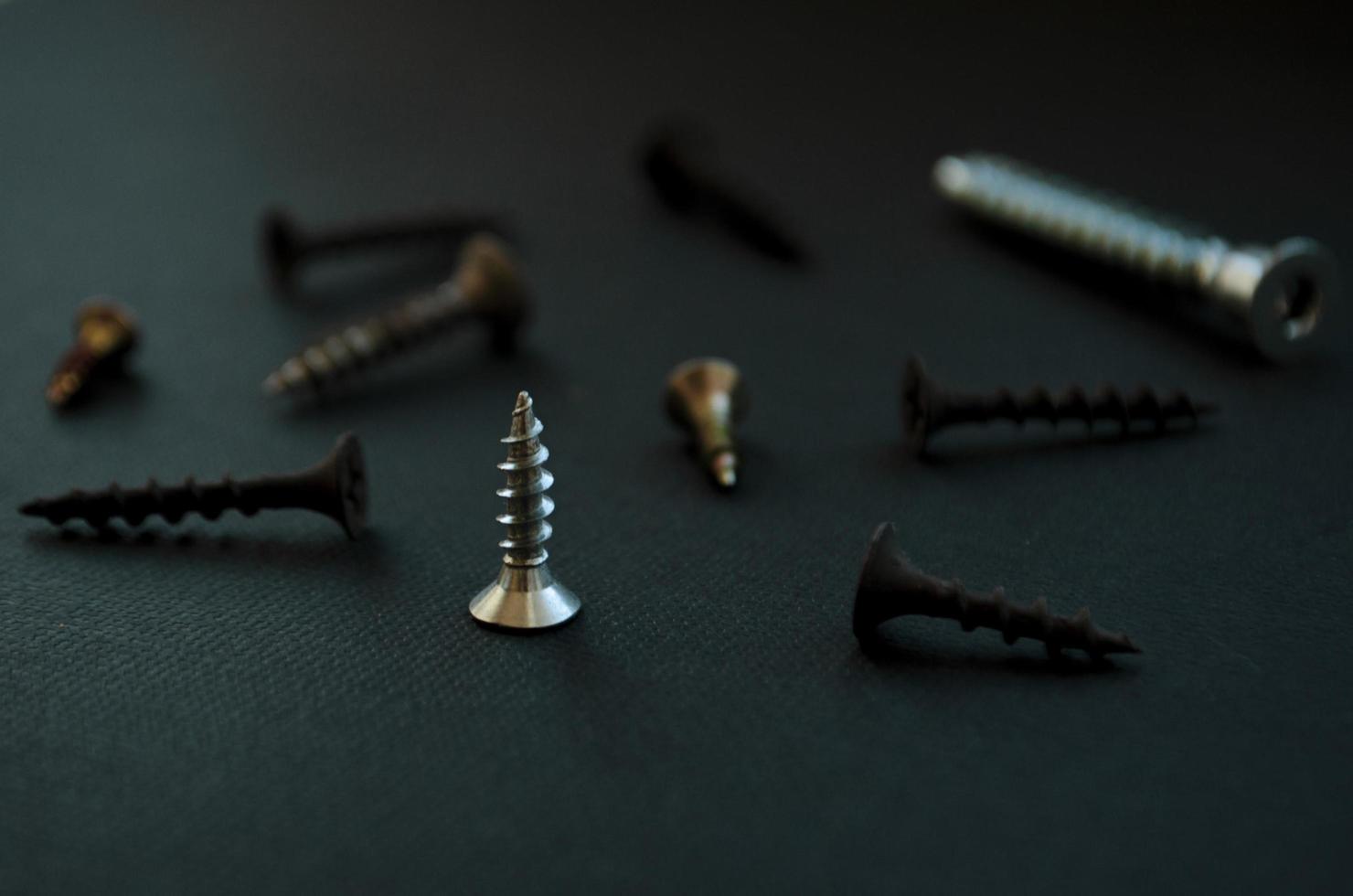 Group of screws on dark green background. Metal screws. Repairing tools. Dark green photo. Technical concept. Close up photo. Repair tools concept. photo