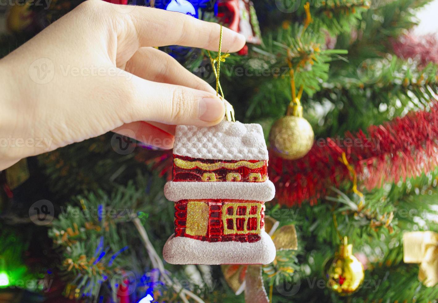 Decorate Christmas tree with toy in the form of little house. Buying a house in the new year. photo