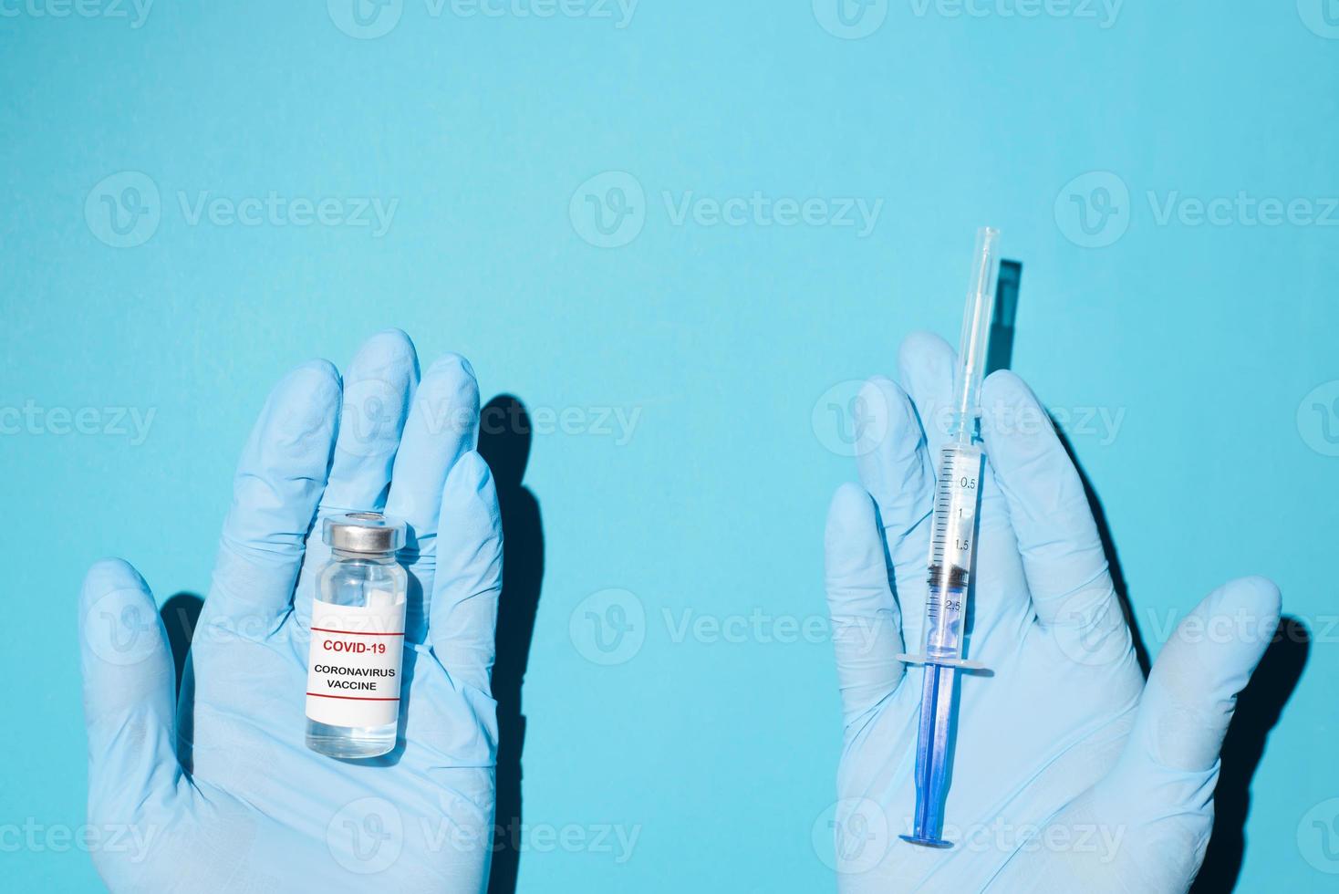 Vaccination concept. Hands in medical gloves holding the covid-19 vaccine and a syringe, top view. photo