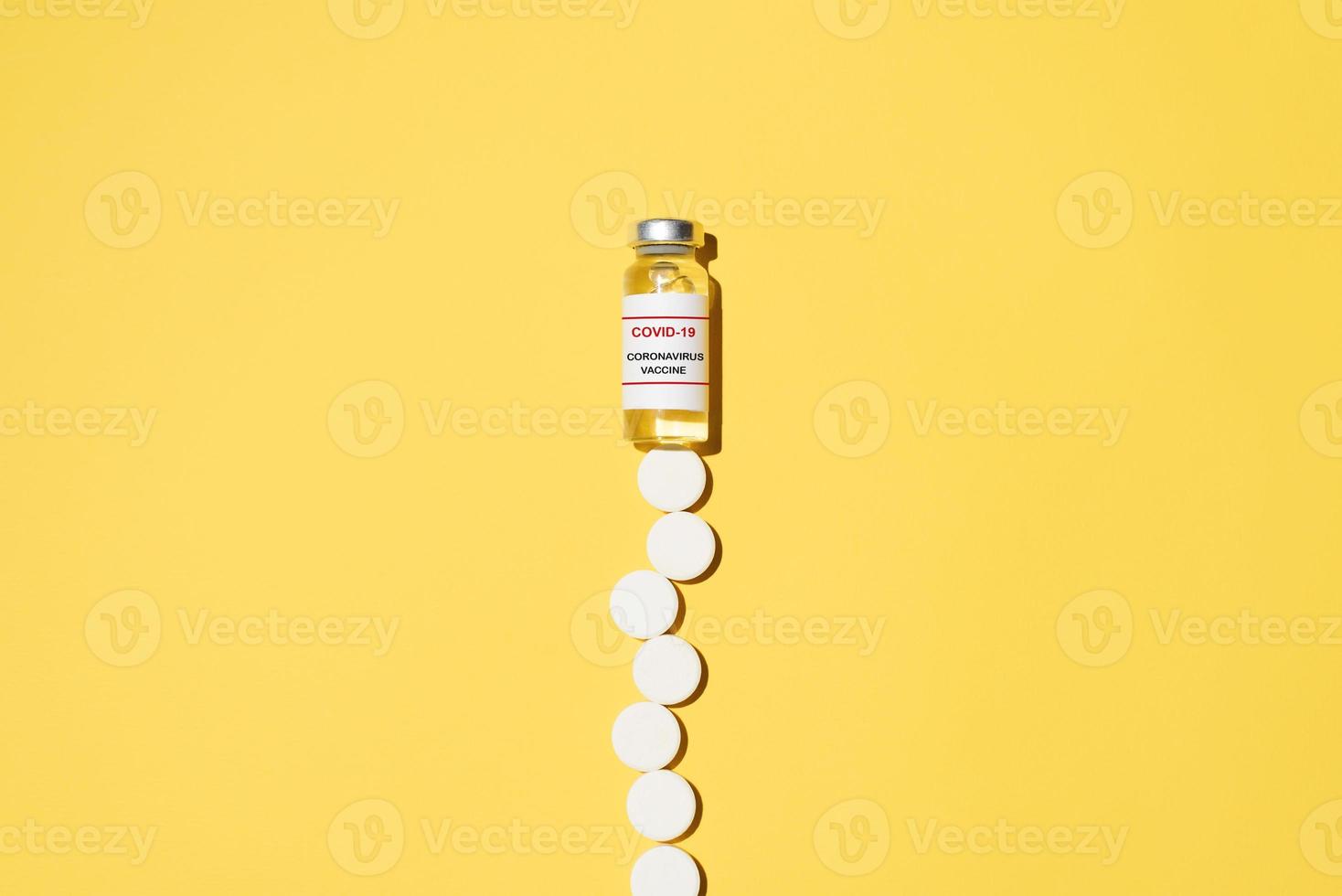 Vaccine vial and many pills on a yellow background. Vaccination and treatment concept. photo