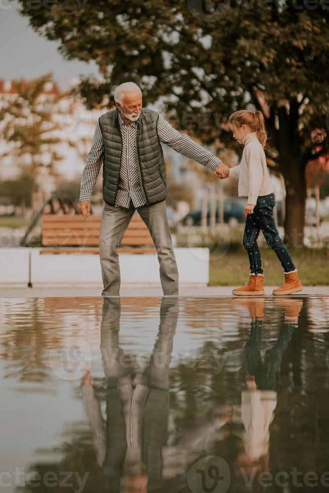 Grandfather spending time with his granddaughter by small water pool in park on autumn day photo