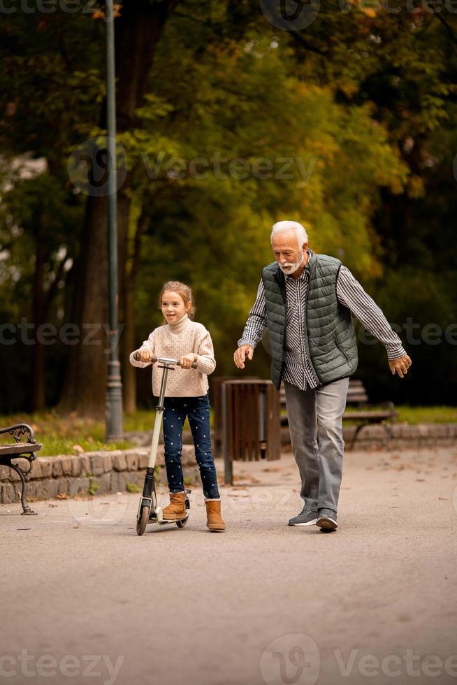 un anciano enseñando a su nieta a andar en patinete en el parque foto