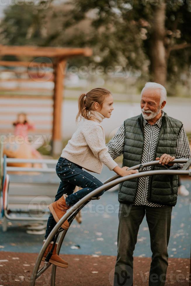 Grandfather spending time with his granddaughter in park playground on autumn day photo