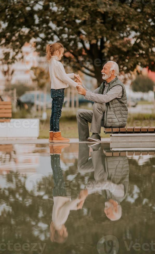 Grandfather spending time with his granddaughter by small water pool in park on autumn day photo