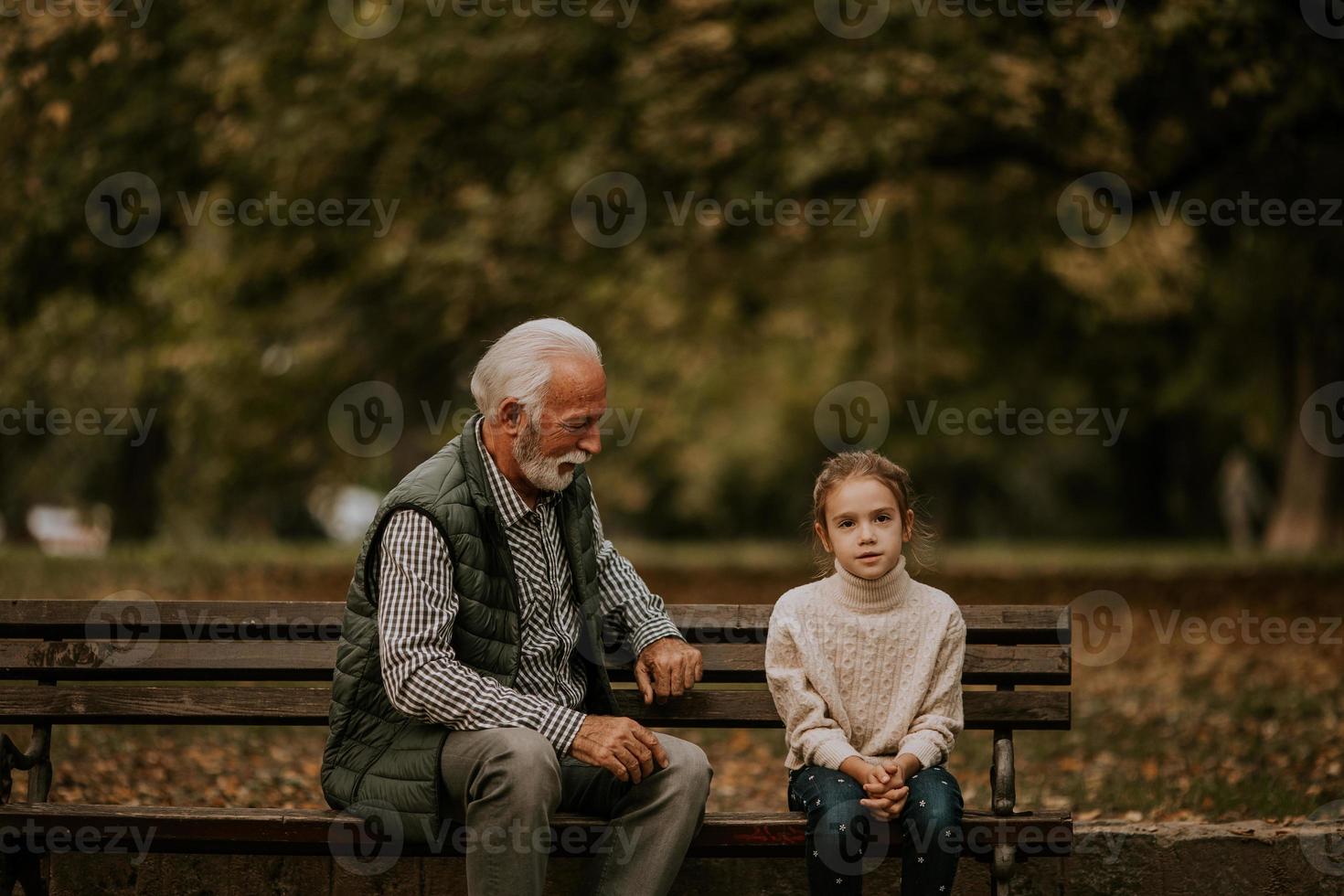 abuelo pasando tiempo con su nieta en un banco en el parque el día de otoño foto