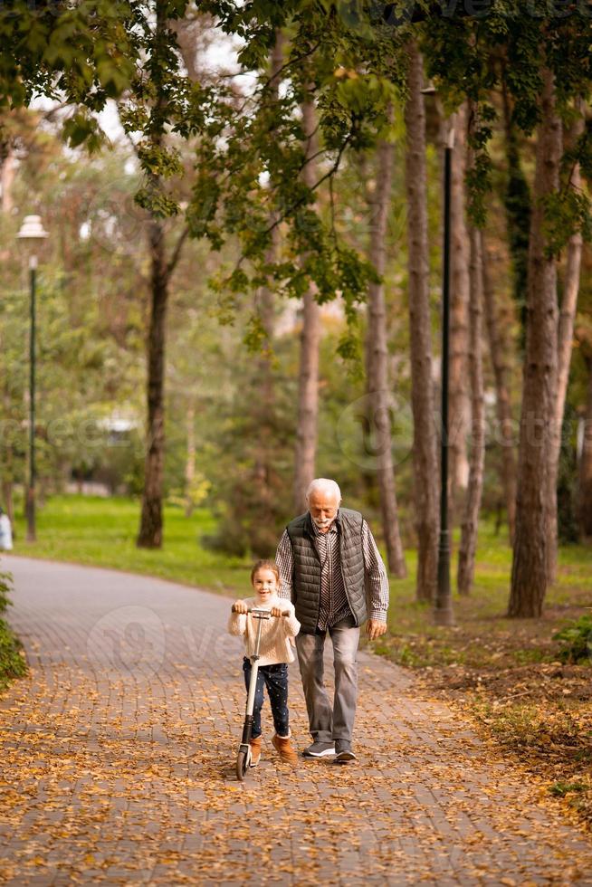 un anciano enseñando a su nieta a andar en patinete en el parque foto