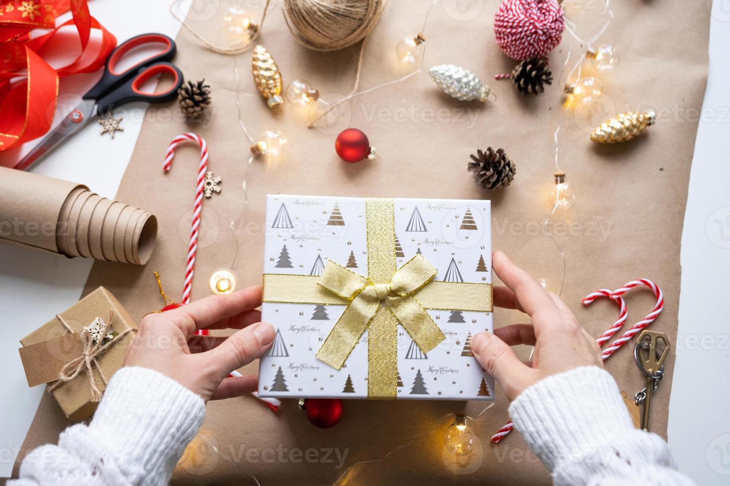 Pack a gift for Christmas and new year in kraft paper, cones, tape, scissors. Tags with mock up, natural decor, hand made, DIY. Festive mood. Flatlay, background photo