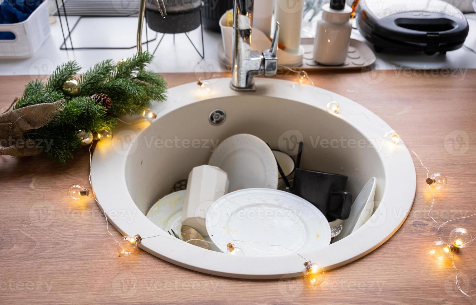 Dirty dishes in the sink in the garlanded kitchen, a holiday after a feast at Christmas. Mess after the guests for the New Year, kitchen cleaning, detergent, cleaning services photo