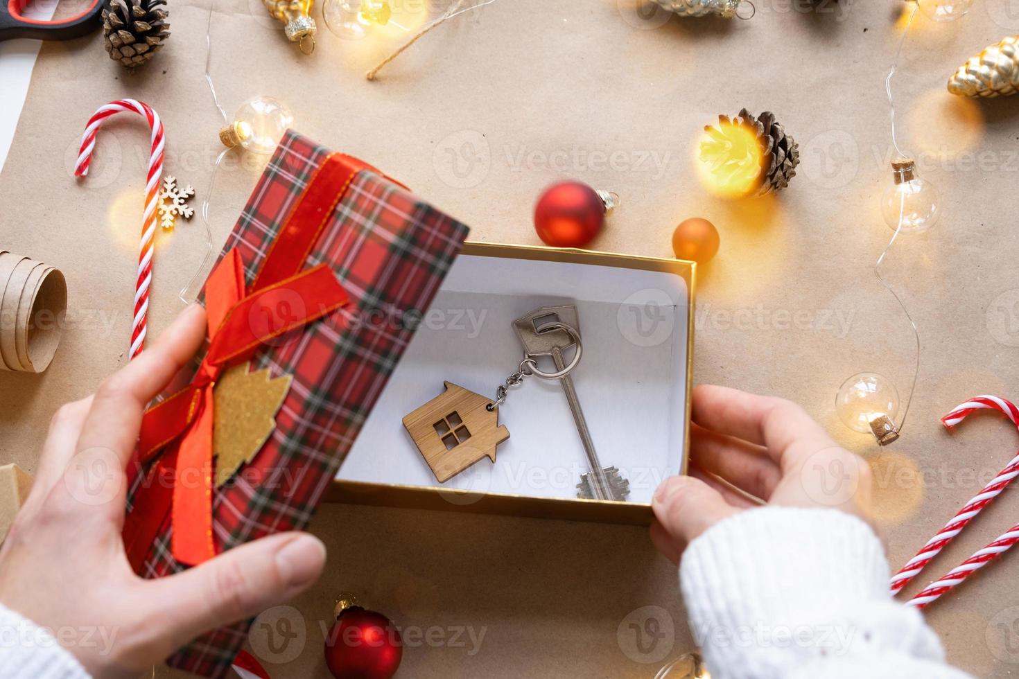 llave de casa con llavero en casa acogedora en caja de regalo con embalaje de decoración navideña. paquete de regalo para año nuevo, navidad. edificio, proyecto, mudanza a casa nueva, hipoteca, alquiler, compra de bienes raíces foto