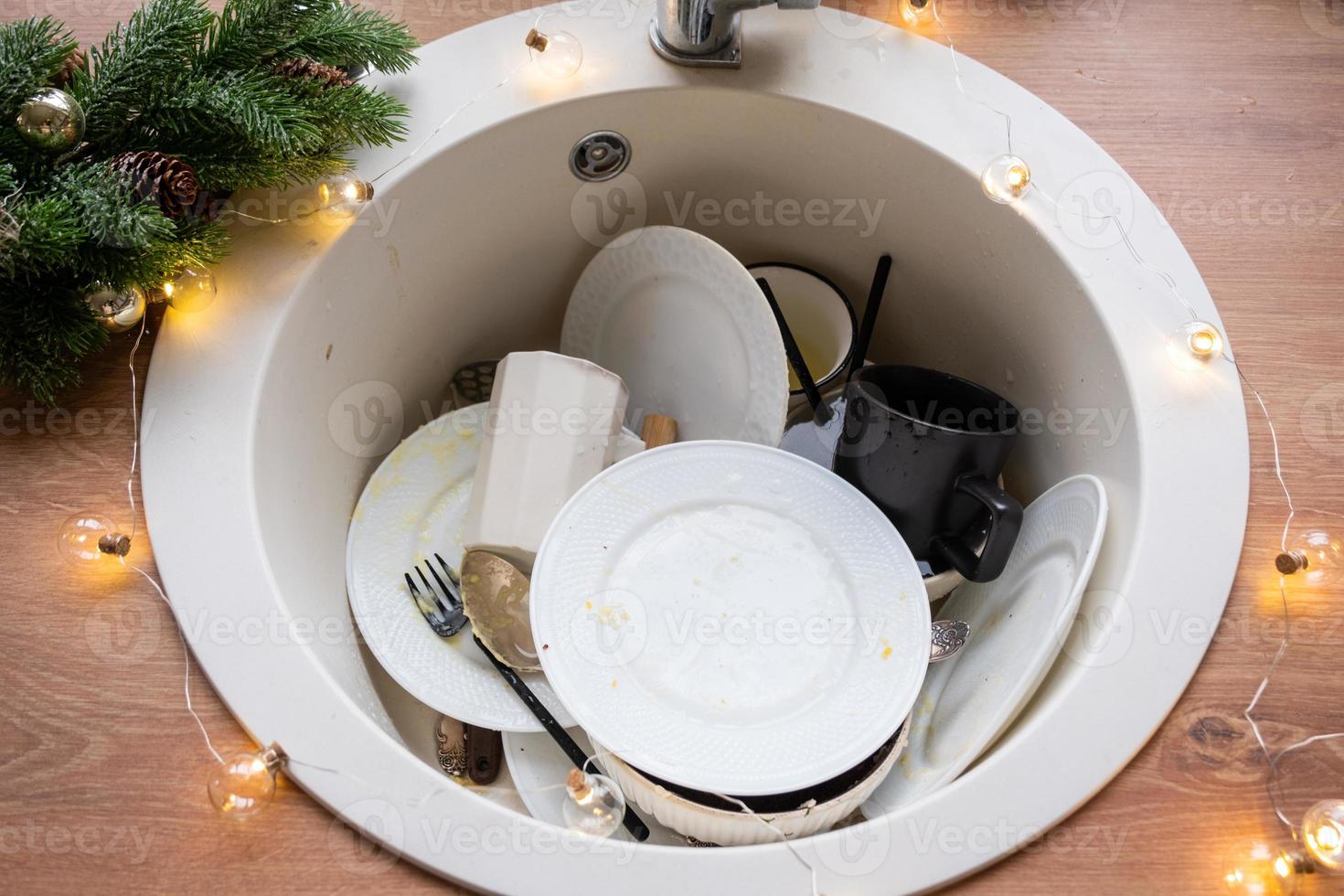 platos sucios en el fregadero de la cocina con guirnaldas, unas vacaciones después de una fiesta en navidad. desorden después de los invitados para el nuevo año, limpieza de cocina, detergente, servicios de limpieza foto