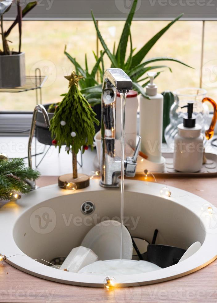 Dirty dishes in the sink in the garlanded kitchen, a holiday after a feast at Christmas. Mess after the guests for the New Year, kitchen cleaning, detergent, cleaning services photo