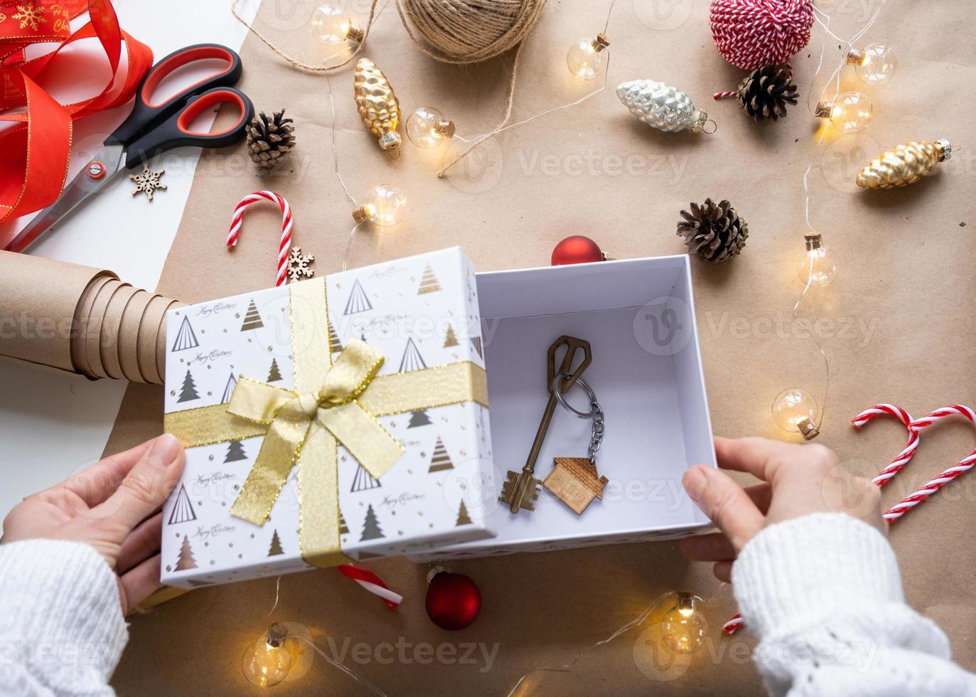 Key to house with keychain on cozy home in gift box with Christmas decor packaging. Pack present for New Year, Christmas. Building, project, moving to new house, mortgage, rent, purchase real estate photo