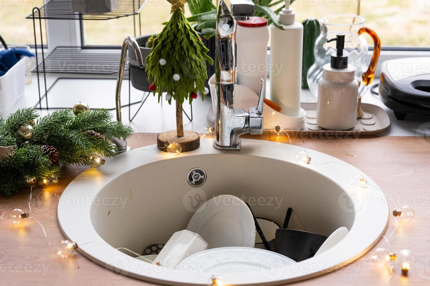 Dirty dishes in the sink in the garlanded kitchen, a holiday after a feast at Christmas. Mess after the guests for the New Year, kitchen cleaning, detergent, cleaning services photo