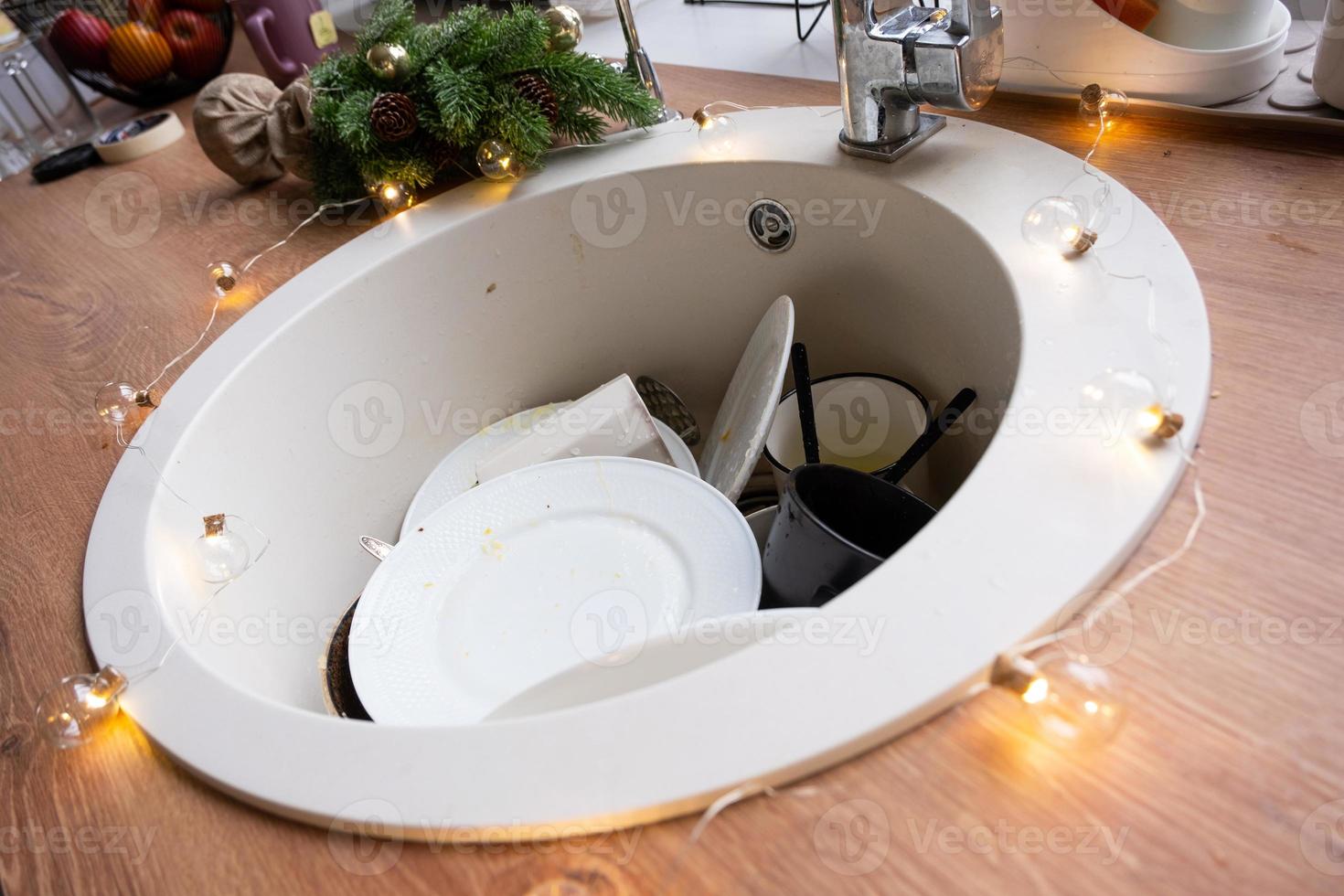 Dirty dishes in the sink in the garlanded kitchen, a holiday after a feast at Christmas. Mess after the guests for the New Year, kitchen cleaning, detergent, cleaning services photo