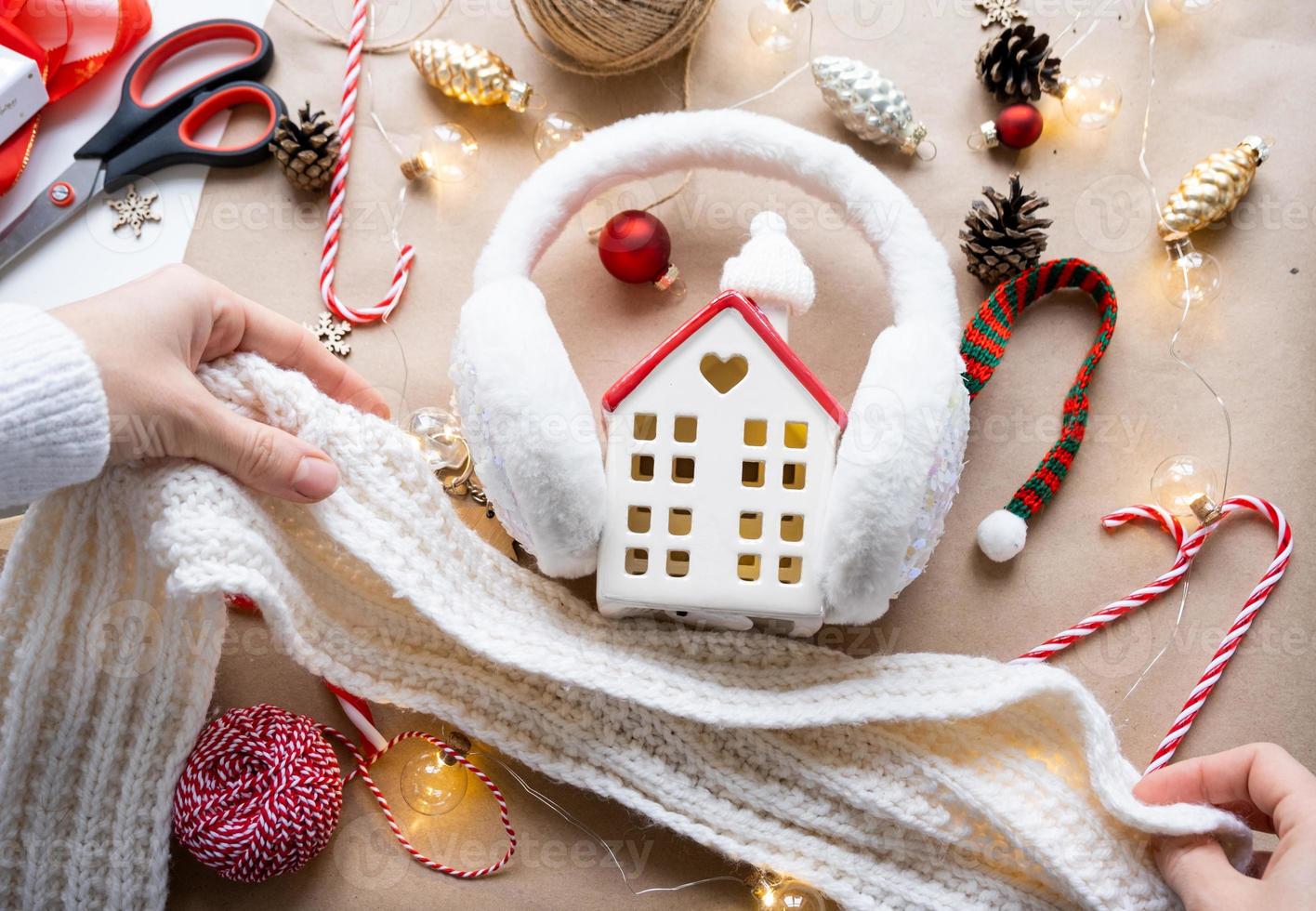 Cozy house in Christmas decor layout, warm knitted scarf, hat, winterization. Winter, snow - home insulation, protection from cold weather, room heating system. Festive mood, Christmas, New Year photo