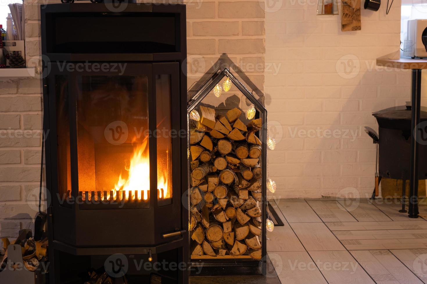 Chimenea de estufa de metal negro con madera en una pila de leña - el interior de una casa de pueblo privada. calefacción y calefacción de la casa con leña, el calor del fuego del hogar. foto