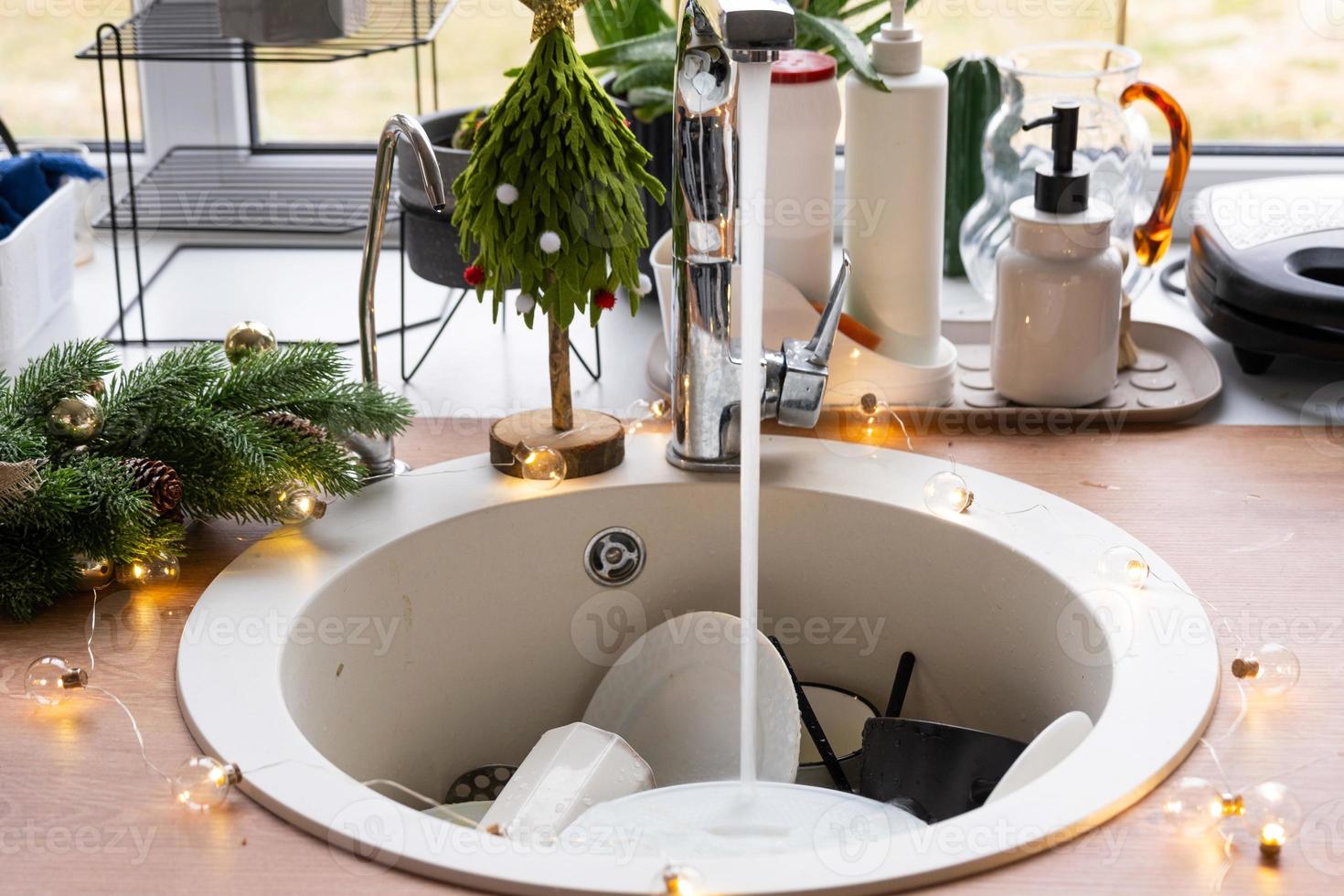 Dirty dishes in the sink in the garlanded kitchen, a holiday after a feast at Christmas. Mess after the guests for the New Year, kitchen cleaning, detergent, cleaning services photo