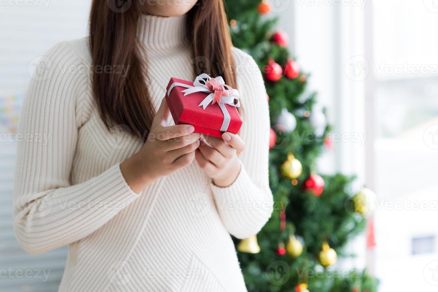 mujer con suéter sosteniendo una pequeña caja de regalo roja sobre fondo blanco foto