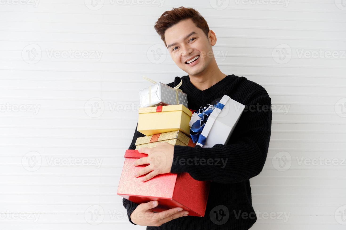 Portrait of a smiling Asian young man holding many gifts box on wall white background photo