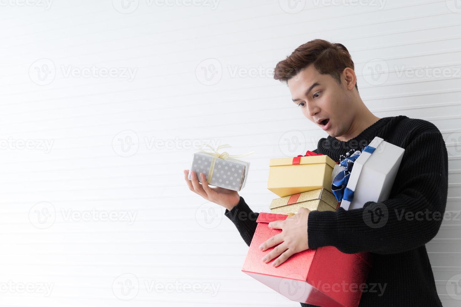 Portrait of a exciting Asian young man holding many gifts box on wall white background photo