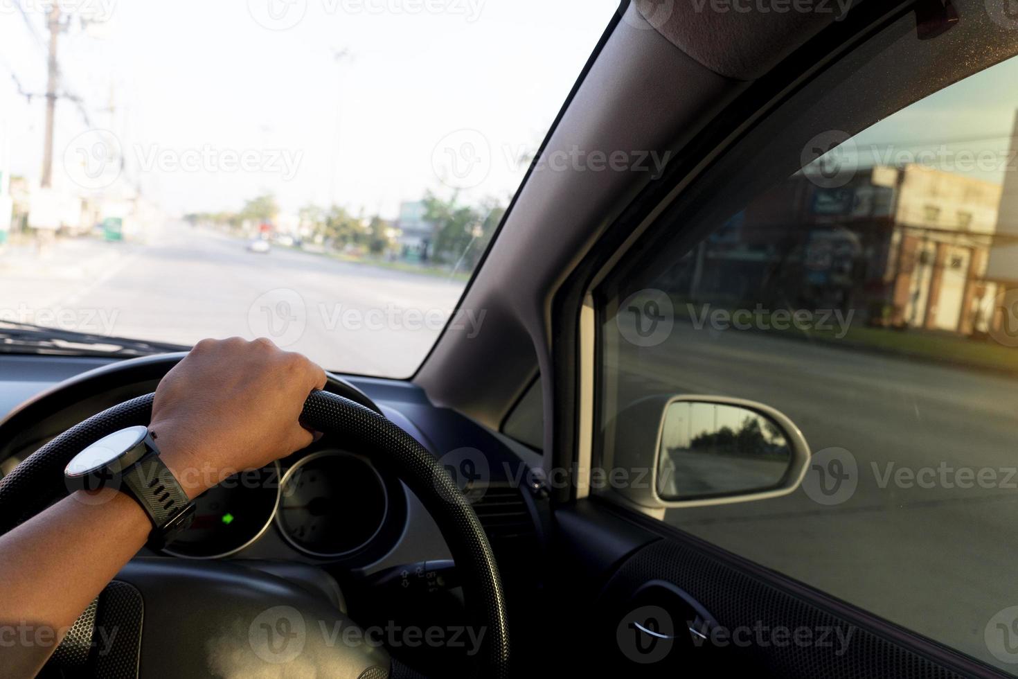 la mano de la gente sostiene el volante a la derecha. conducir dentro del automóvil en la carretera vacía durante el día. borrosa de la ciudad al lado de la carretera en Tailandia. foto