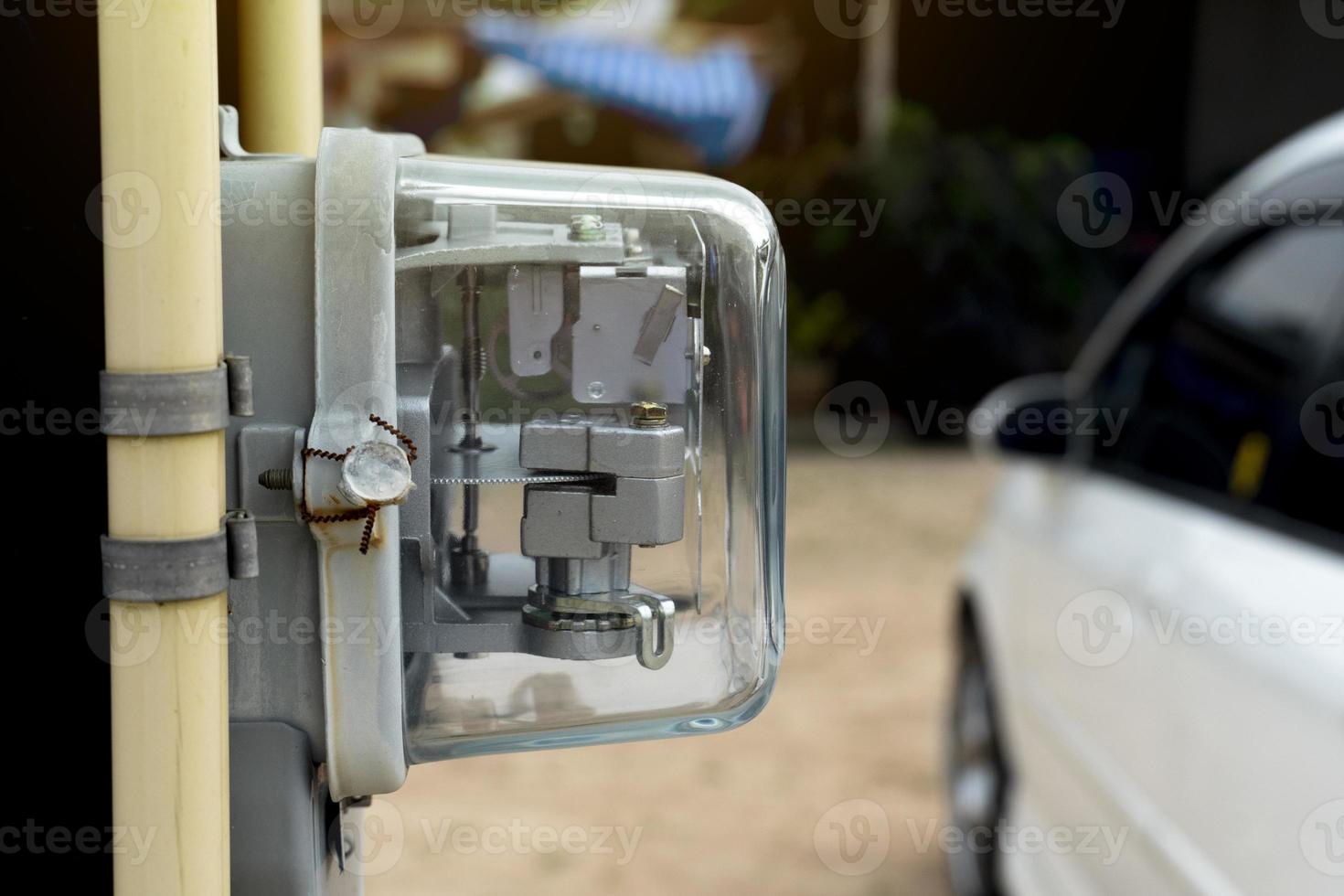 Front view of Power meter of Thailand attached to outdoor power pole. with yellow pipe beside of volt meter. and blurred of car parking on the ground. photo