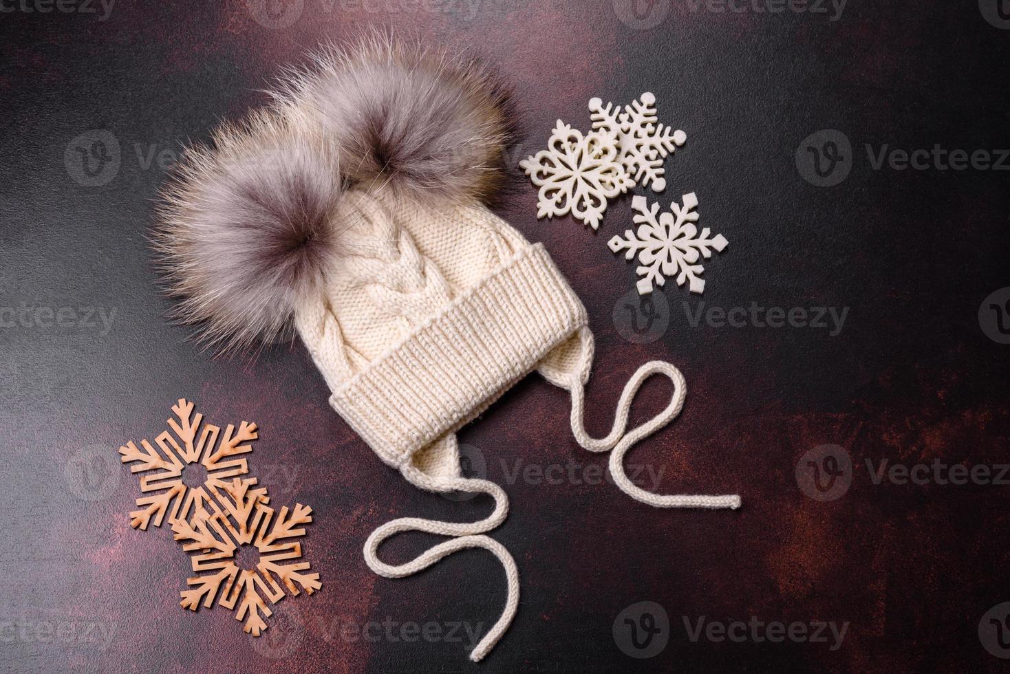 Beautiful white knitted winter cap with pompons on a dark concrete background photo