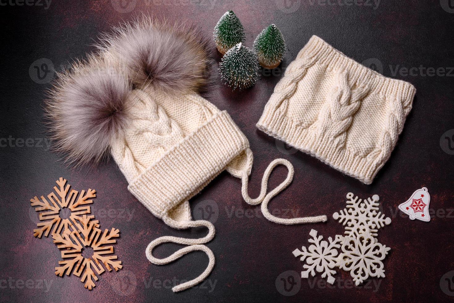 Beautiful white knitted winter cap with pompons on a dark concrete background photo