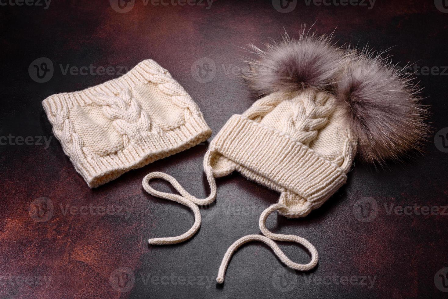 Beautiful white knitted winter cap with pompons on a dark concrete background photo