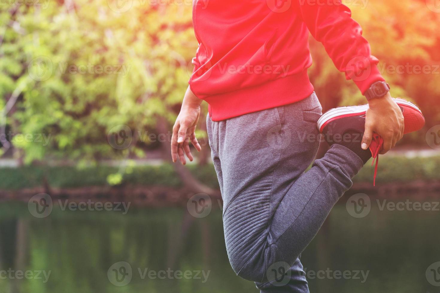 young man runner stretching for warming up before running or working out on road in the park. Track and Field Athlete exercise. Fitness and healthy lifestyle concept. photo