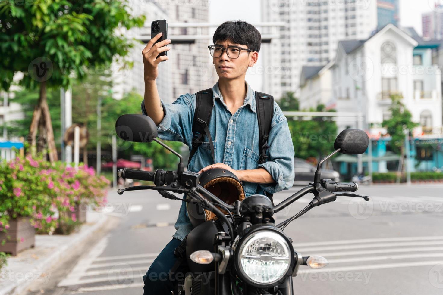 image of asian man, sitting on moto using mobile phone photo