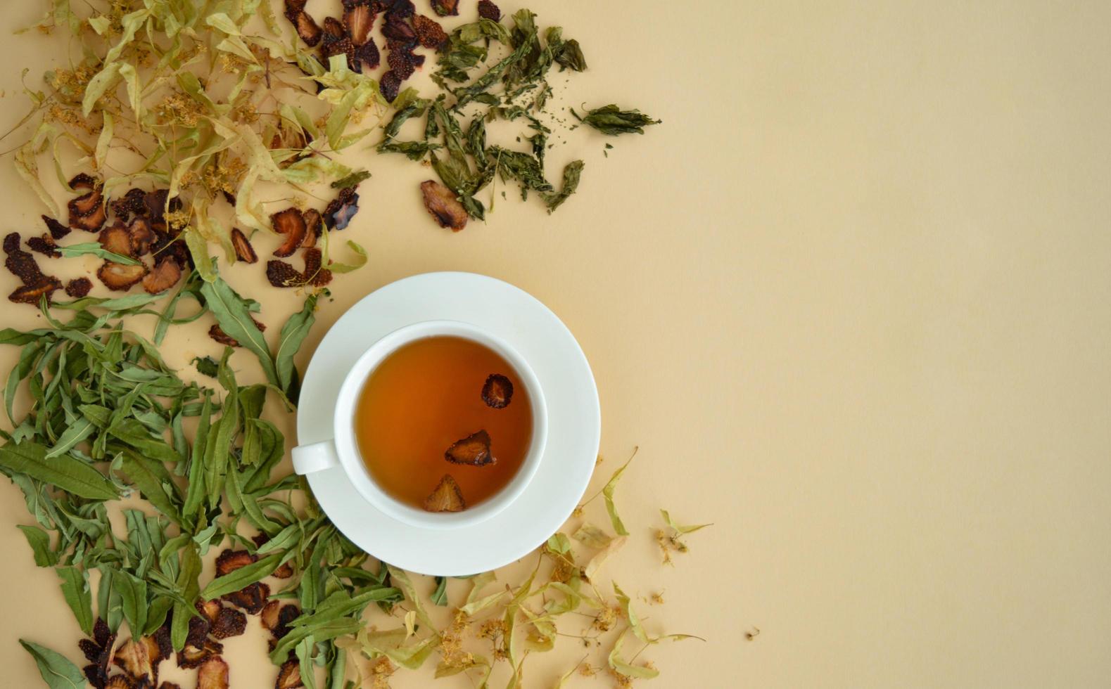 té de hierbas en una taza blanca para la belleza y la salud, hierbas secas, flores de tilo y fresas yacen alrededor. foto
