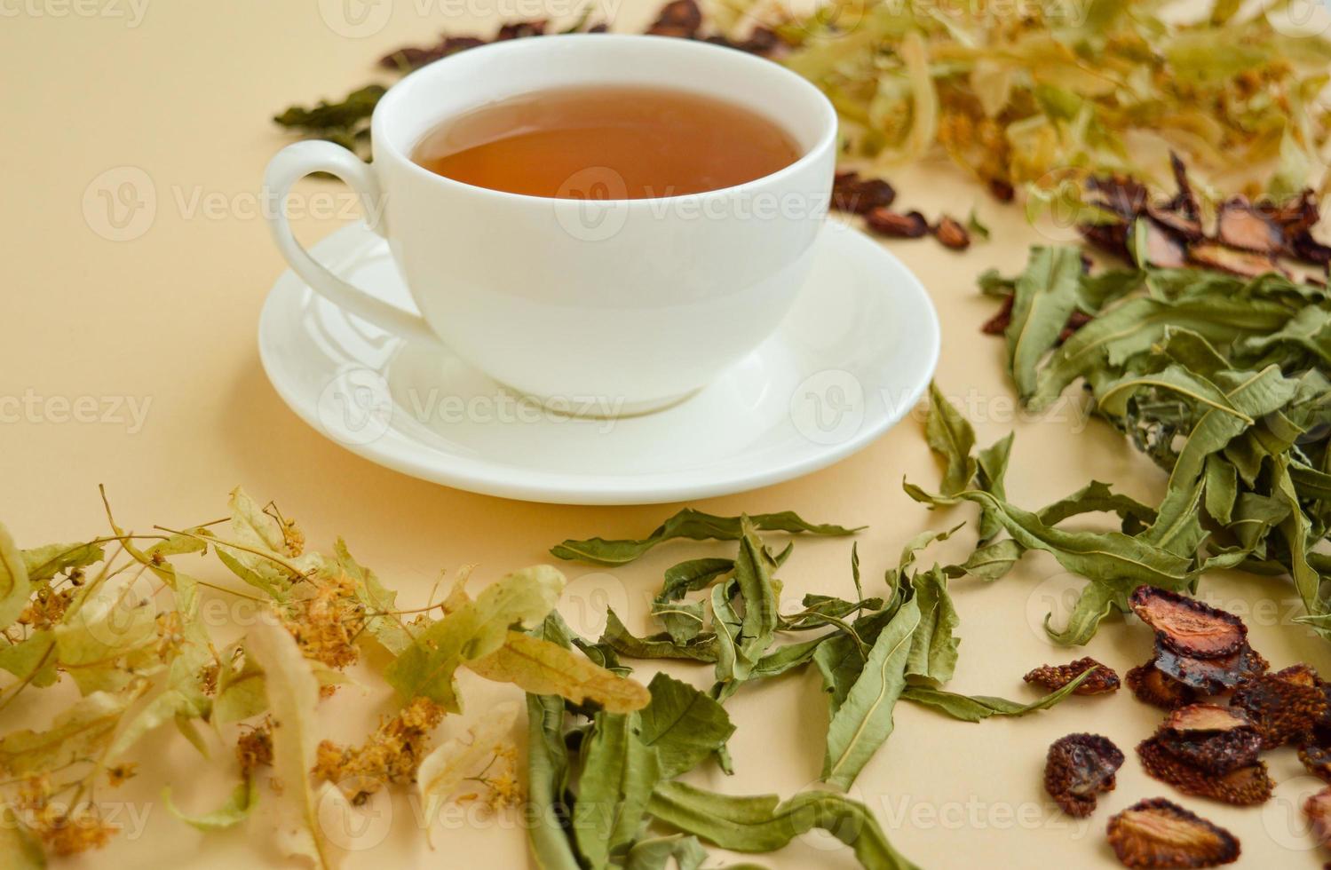 herbal tea in a white cup for beauty and health, dried herbs, linden flowers and strawberries lie around. photo