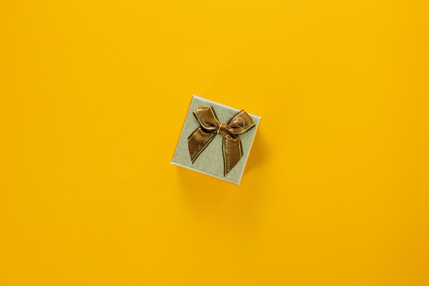 Mini golden gift box with ribbon on yellow background, giving special gift box for Merry New Year and Merry Christmas 2023 concept, yellow gift box on top view. photo