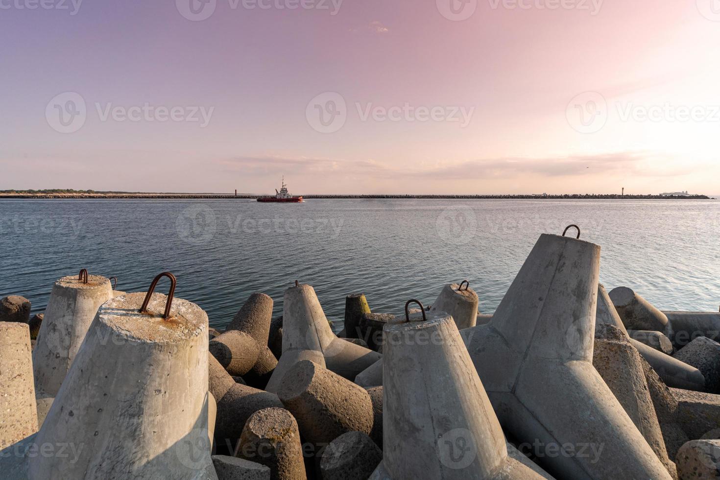 Tugboat sailing in sea to tow ship to port. Tetrapod breakwaters in harbor. Beautiful sunset over the pier. photo