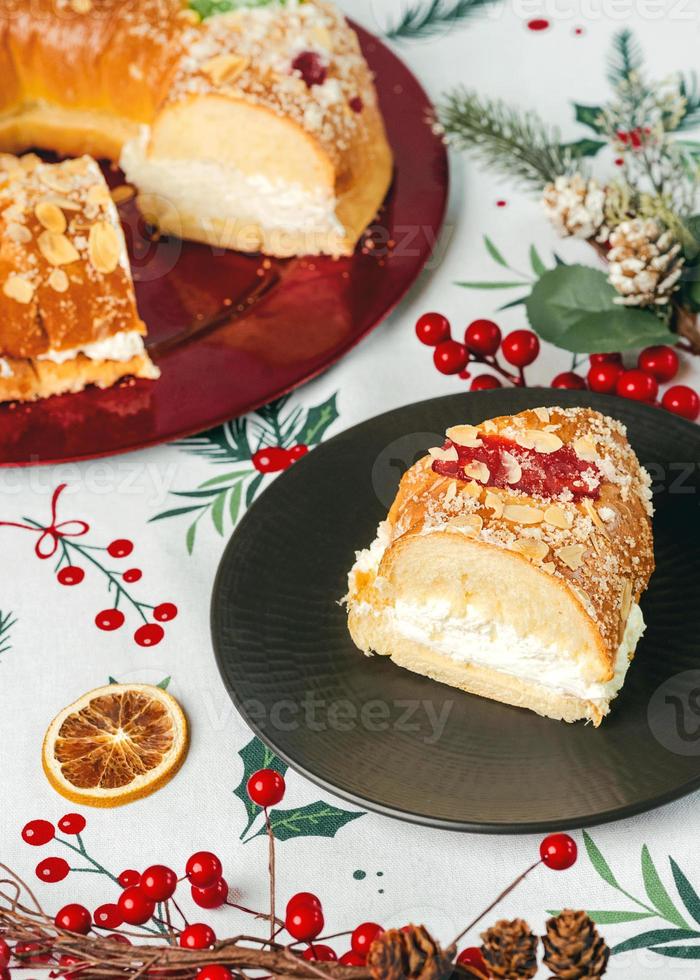 Roscon de reyes with cream and christmas ornaments on a red plate. Kings day concept spanish three kings cake.Typical spanish dessert for Christmas photo