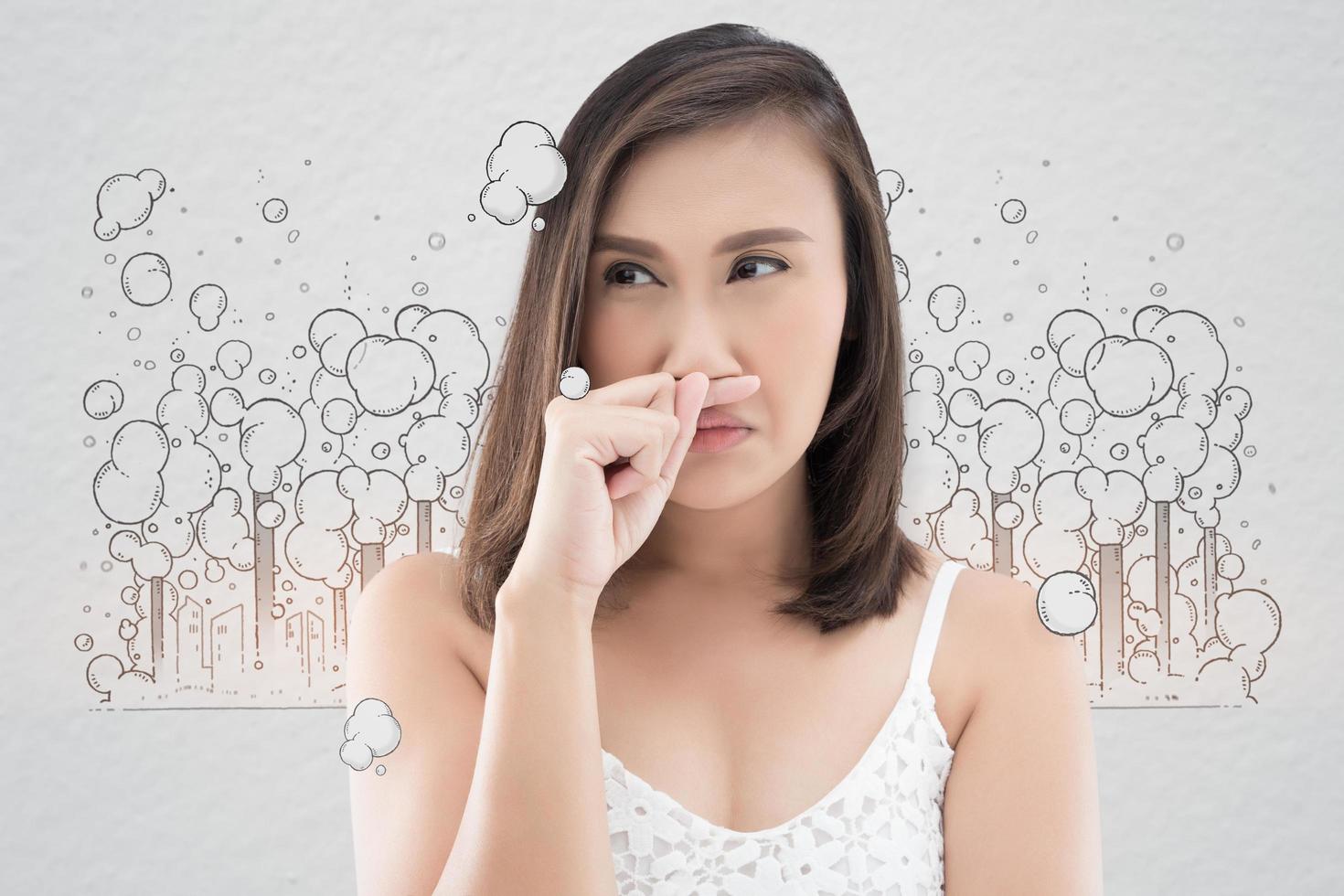 Asian woman in white dress catch her nose because of a bad smell against gray background photo