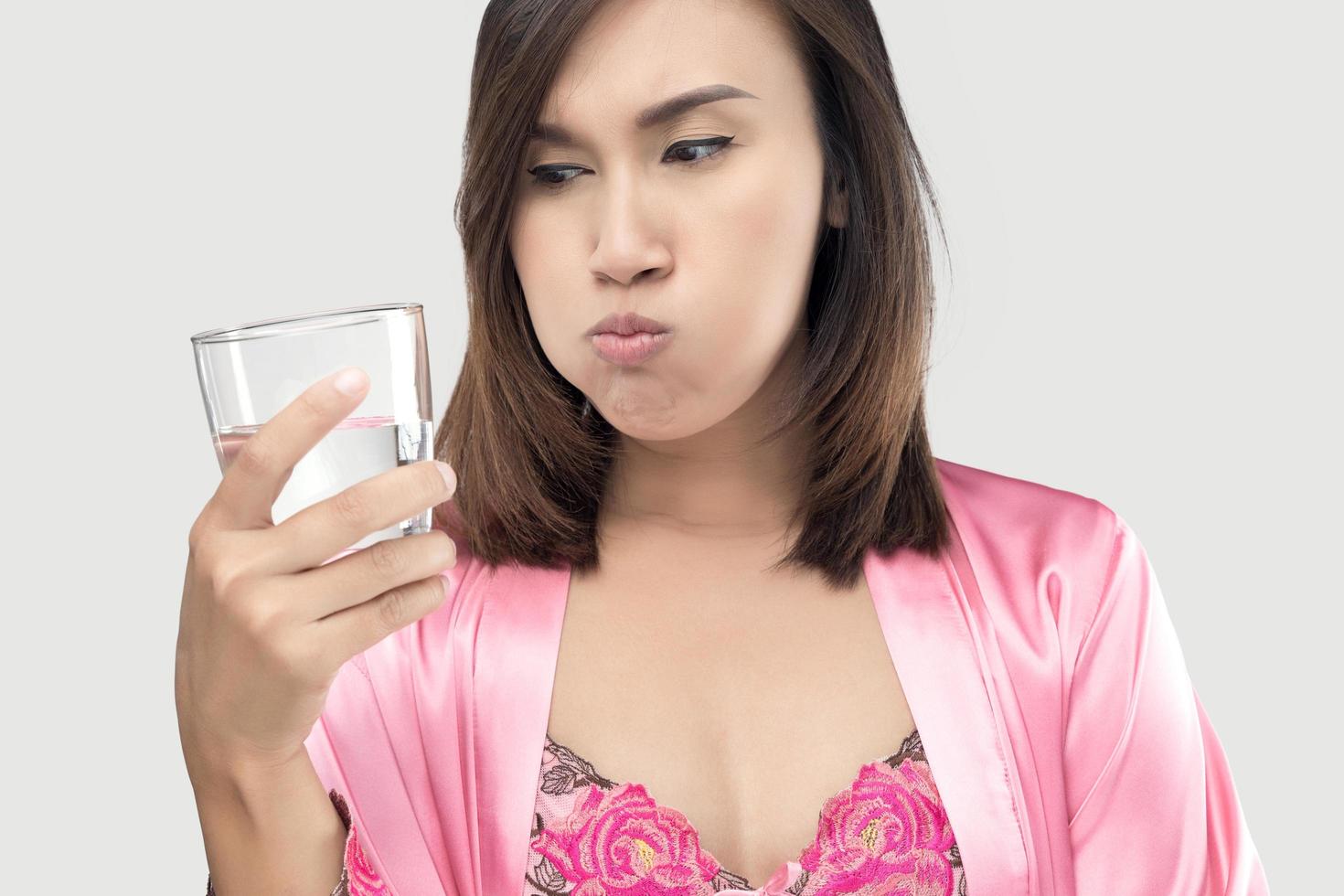 Asian woman rinsing and gargling while using mouthwash from a glass against gray background. photo
