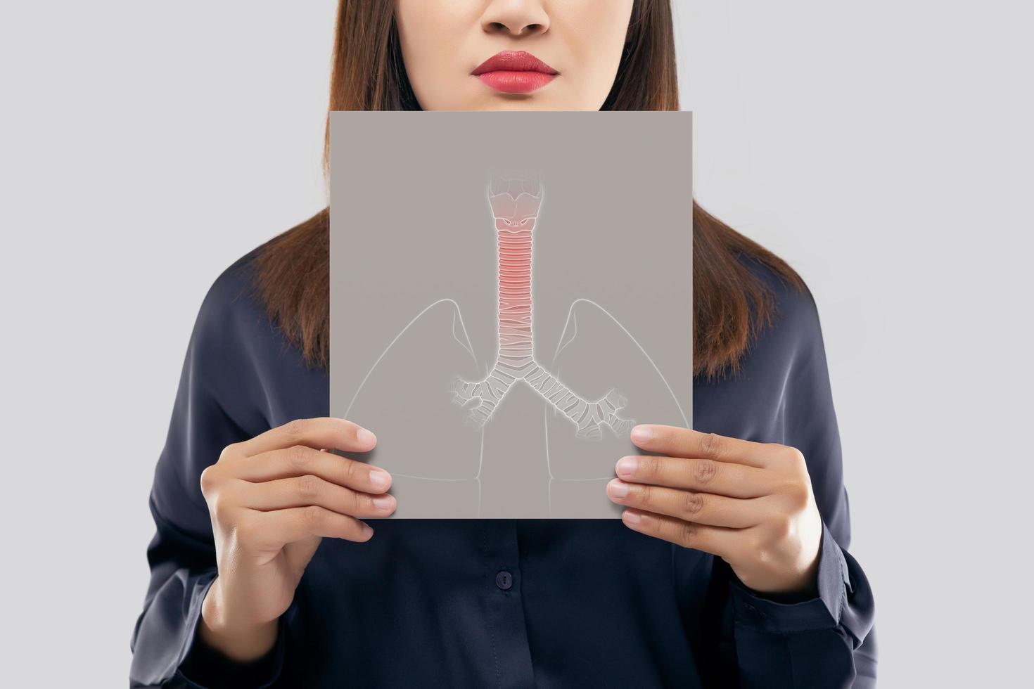 mujer asiática sosteniendo una tráquea de papel blanco y una imagen de los pulmones de su boca contra el fondo gris. síntomas de bronquitis. concepto con atención médica y medicina. foto