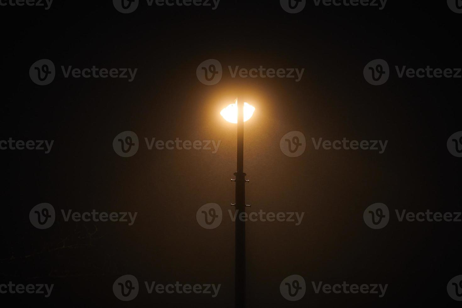 una farola nocturna brilla con una tenue y misteriosa luz amarilla a través de la niebla nocturna foto