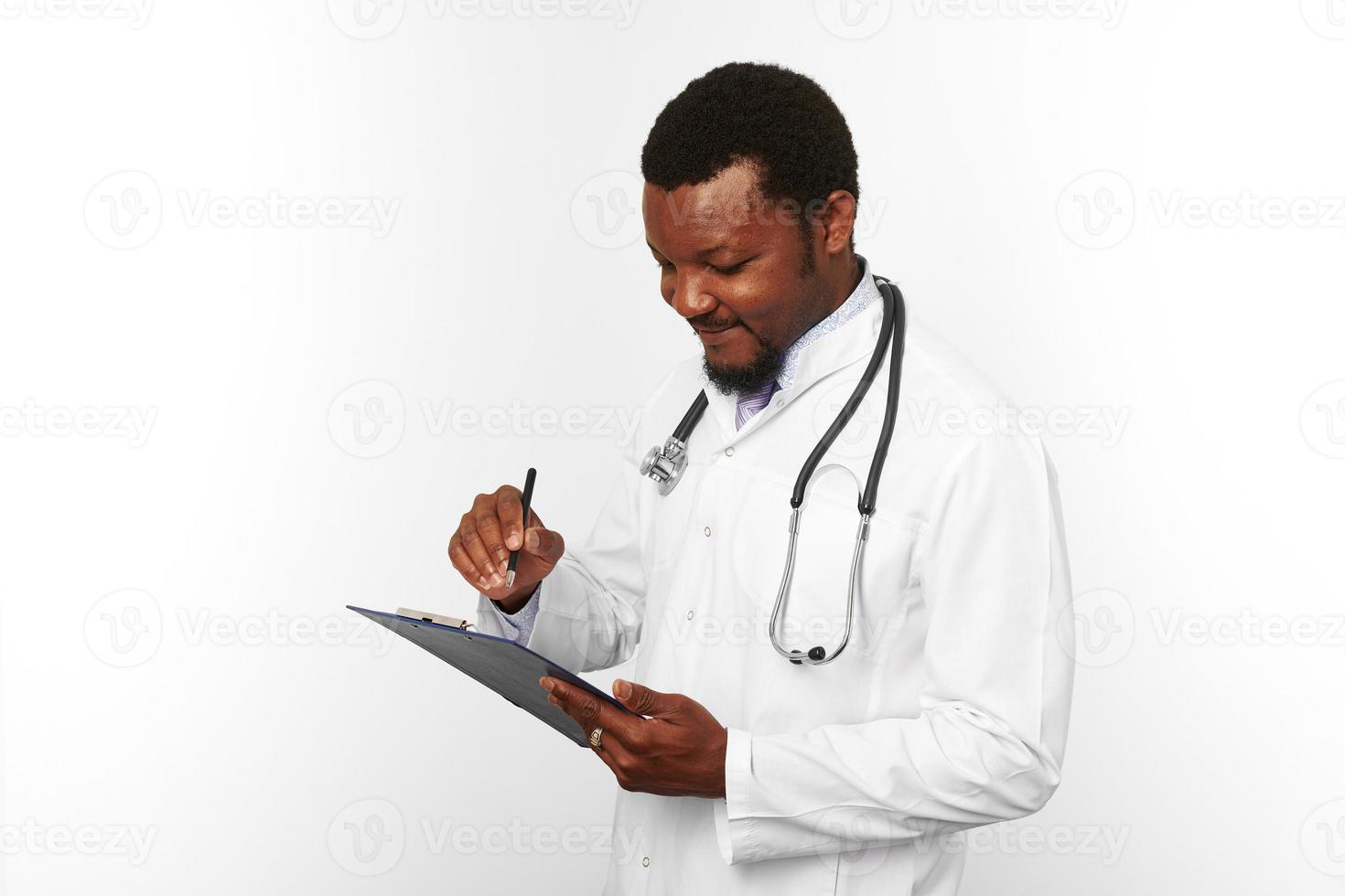 Black bearded doctor man in white coat with stethoscope filling medical records on clipboard photo