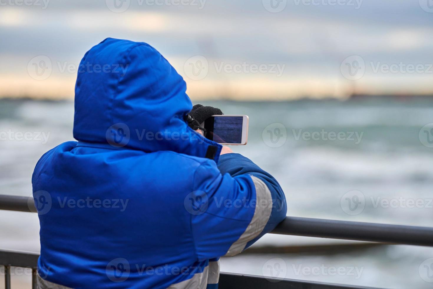 Back view of man tourist taking photo of sea with smartphone