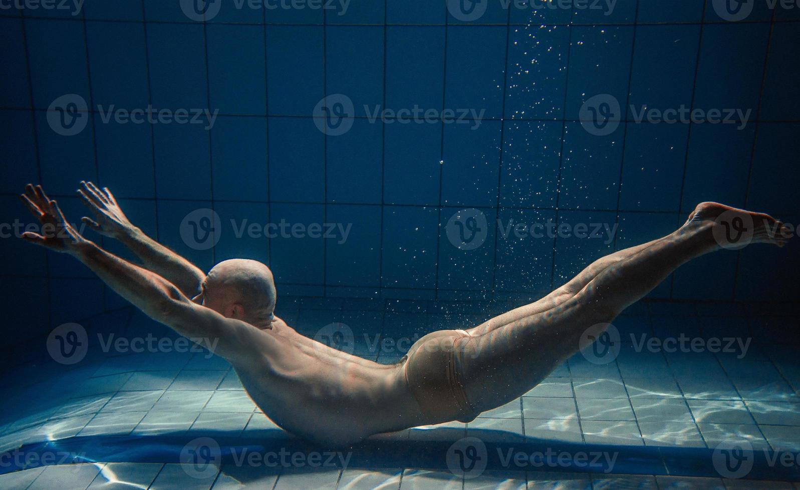 hombre de deporte atlético bajo el agua en la piscina. deportes, yoga, concepto de buceo libre foto