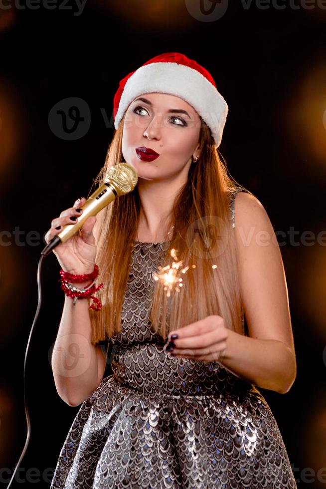 young blonde attractive woman in red new year hat with microphone and sparkler on singing the stage photo