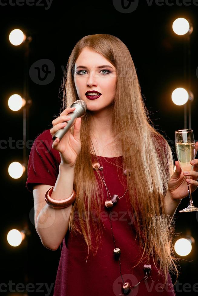 retrato de una hermosa y atractiva mujer rubia sonriente cantando en el micrófono en el karaoke en el escenario foto