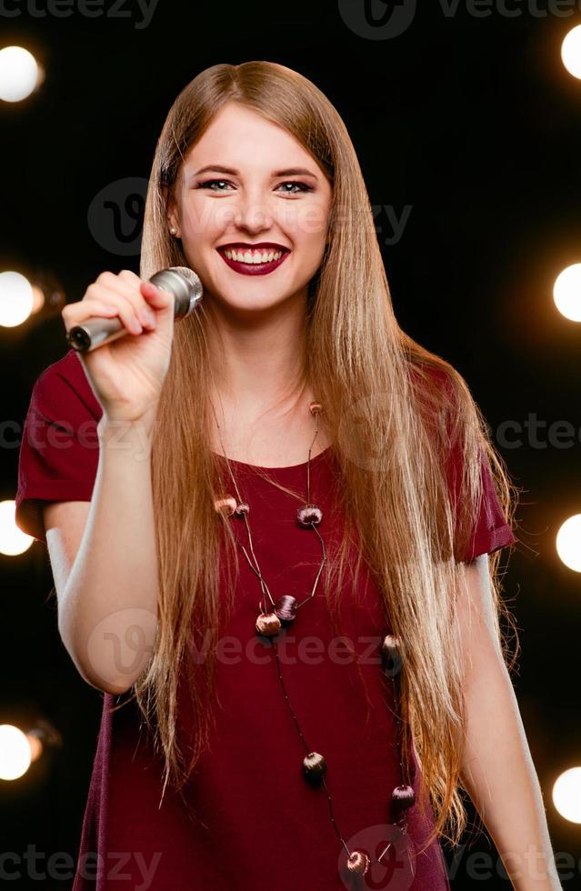 Portrait of beautiful attractive smiling blonde woman singing in microphone in karaoke on the stage photo