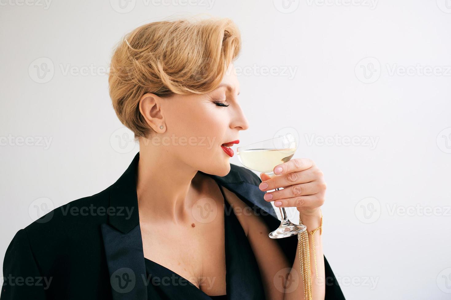 Laughing Caucasian mature stylish elegant woman in tuxedo with glass of sparkling wine. Party, celebration, anti age concept photo